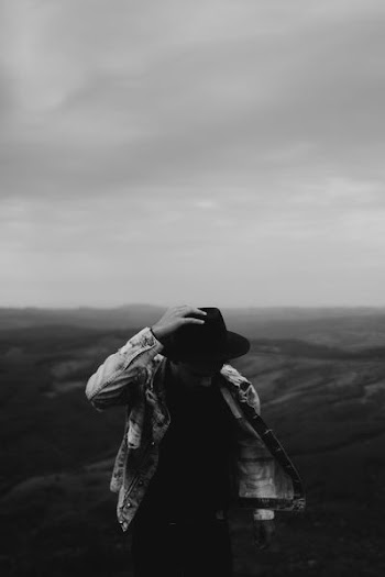 grayscale photography of man holding his hat