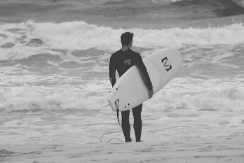 grayscale photography of man in black wetsuit while carrying surfboard near sea
