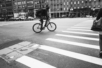 grayscale photography of man riding bicycle crossing pedestrian lane