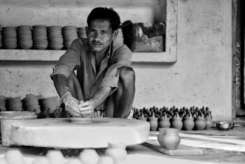 Grayscale Photography of Man Sitting Near Clay Pots