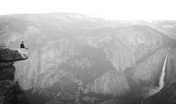grayscale photography of person sitting on rock and waterfalls during daytime