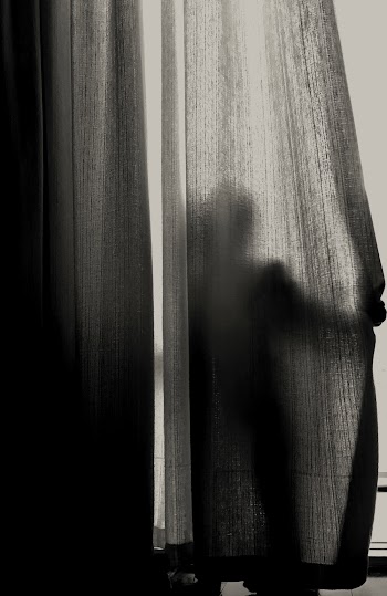 Grayscale Photography of Person Standing While Hiding on Curtain