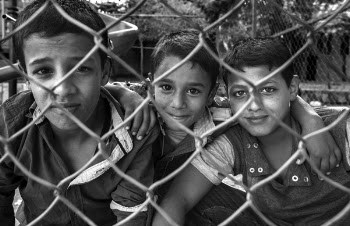 Grayscale Photography of Three Boys Beside Steel Fence