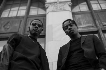 Grayscale Photography of Two Men Standing Near Building