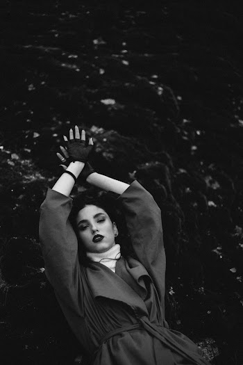 Grayscale Photography of Woman Wearing Coat Near Rock Foramation