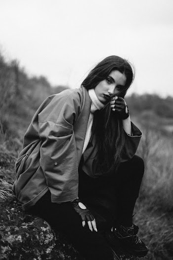 Grayscale Photography of Woman Wearing Jacket Sitting on Rock