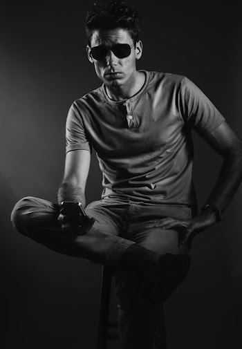 Grayscale Studio Photo of Man Wearing T-shirt Sitting on Stool Holding Smartphone