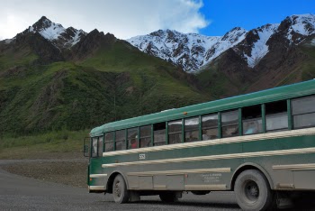 Green and White Buss on Gray Concrete Top Road Across Green Mountains Under Cloudy Sky