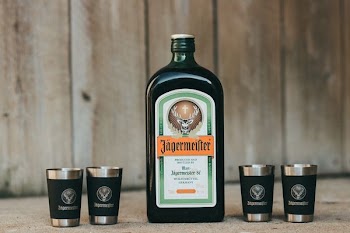 green and white glass bottle beside four stainless steel drinking cups