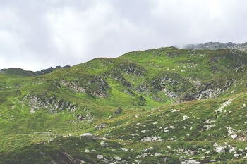green grass field on mountain under cloudy sky at daytime