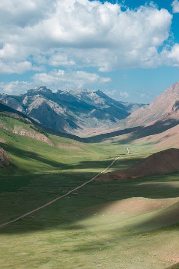 green grass field valley under white clouds during daytime