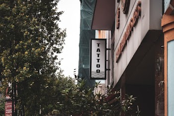 Green Trees In Front Of A Building With A "Tattoo" Signage Hanging Outside