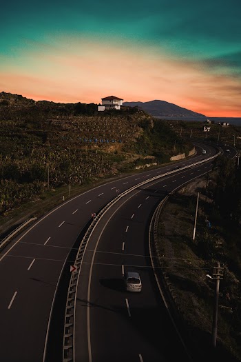 Grey Car Traveling on Swerving Highway Under Green and Orange Sky