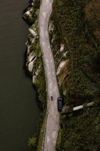 Grey Road Near Body of Water and Green Field