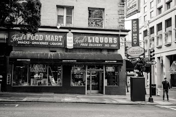 Greyscale Photo of Man Standing on Road Near Fred's Liqours Building