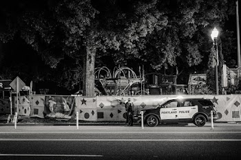 Greyscale Photo of Two Policemen Standing Infront of a Parked Police Car 