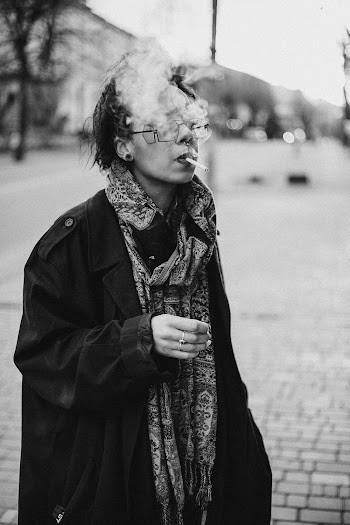 Greyscale Photo of Woman Wearing Coat and Smoking Outside