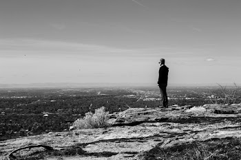 Greyscale Photography of Man Standing on Cliff in Front of Building