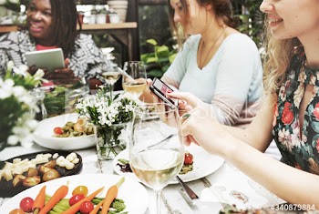 Group of diverse women having meal together using digital devices