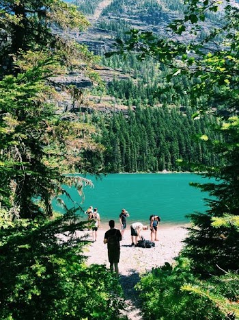 group of people standing beside trees and lake near mountain