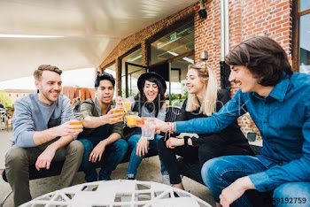 Group of smiling young friends toasting glasses of drink in bar