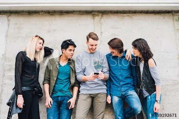 Group of young friends using smartphone while leaning on wall