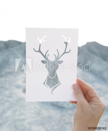 Hand holding perforated paper moose art with mountain background