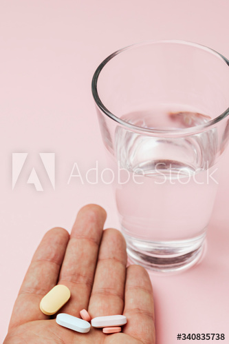 Hand of patient with pills and a glass of water