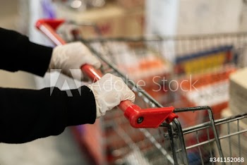 Hand wearing a latex glove while pushing a shopping cart to prevent coronavirus contamination