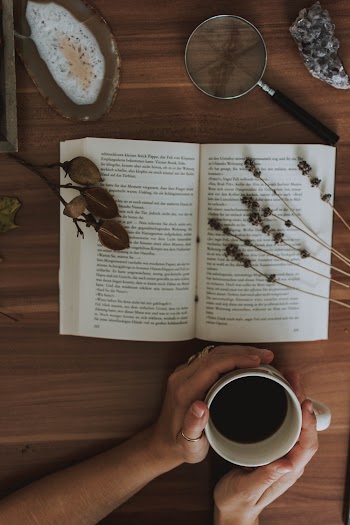 Hands Holding a Cup of Coffee and an open book  in front