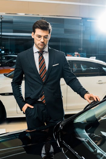 Handsome businessman in eyeglasses choosing car in dealership salon