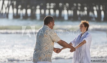Happy active senior couple holding hands on sunny ocean beach