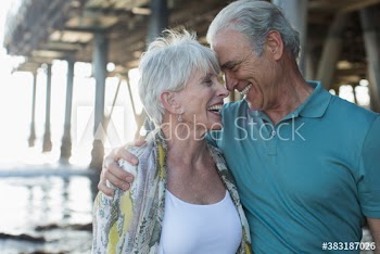 Happy active senior couple hugging on beach below pier