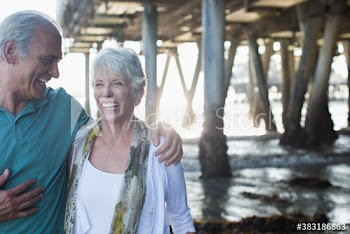 Happy active senior couple on ocean beach below pier