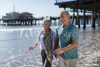 Happy active senior couple wading in sunny ocean surf