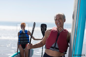 Happy active senior couple with paddleboards in sunny ocean
