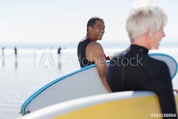 Happy active senior couple with surfboards on sunny beach