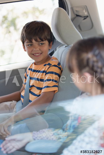 Happy brother and sister riding in backseat of car