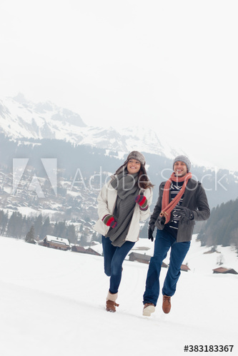 Happy couple couple running in snowy mountain field