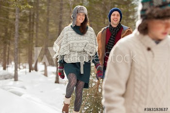 Happy couple dragging Christmas tree in snowy woods