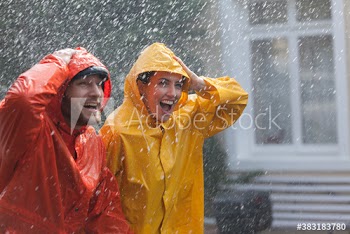 Happy couple in raincoats walking in rain