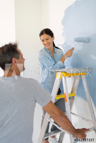 Happy couple painting wall with blue paint