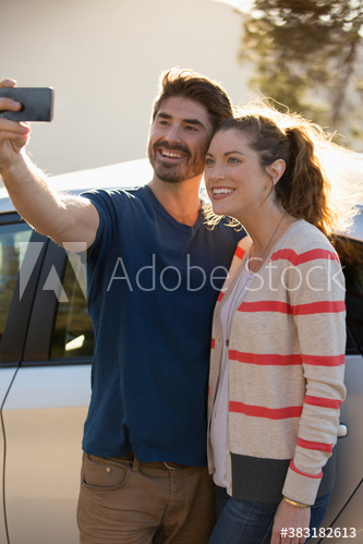 Happy couple taking selfie outside car