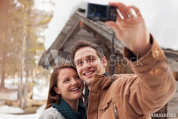 Happy couple taking selfie with digital camera outside cabin