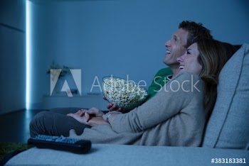 Happy couple watching movie and eating popcorn on sofa