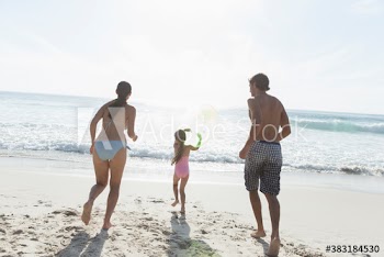 Happy family running toward ocean on sunny beach