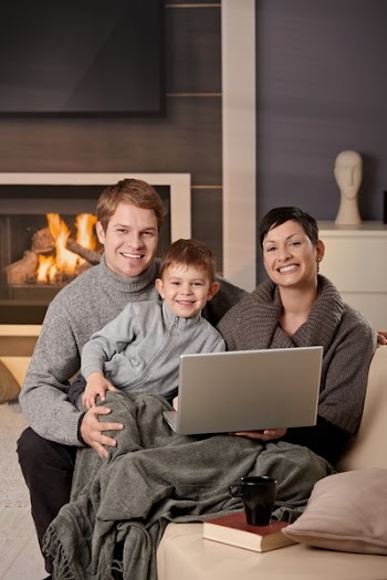 Happy family sitting on couch at home in winter, using laptop computer, looking at camera, smiling.