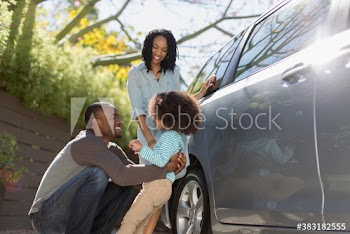 Happy family standing outside car in sunny driveway