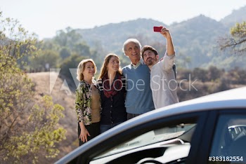 Happy family taking selfie outside car at sunny roadside