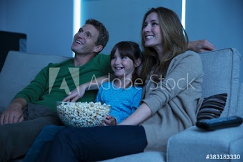 Happy family watching movie and eating popcorn on sofa